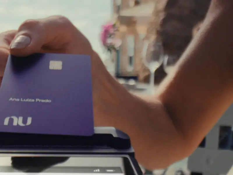 Pessoa segura cartão do Nubank em ambiente interno, representando o uso de serviços do banco digital.