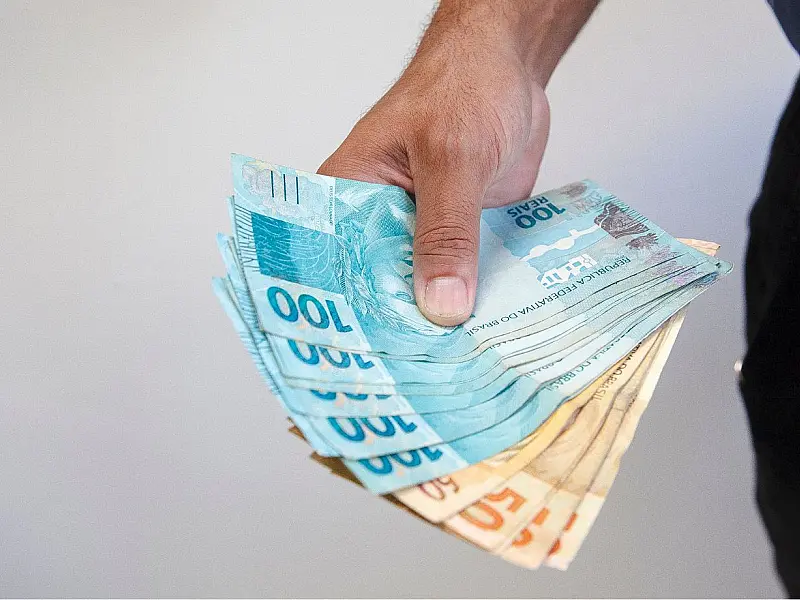 Notas de real brasileiro espalhadas sobre mesa representando pagamento de benefício.