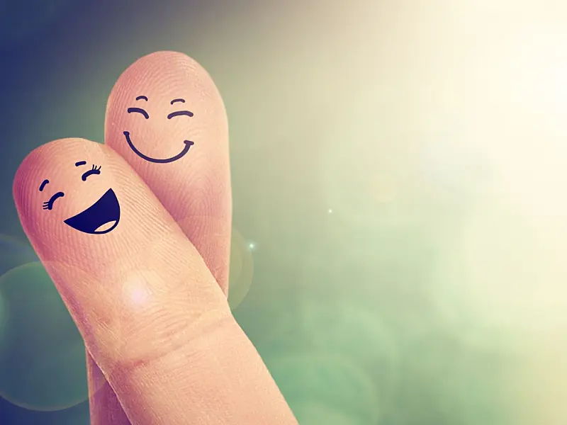 Dedos com desenhos de rostos felizes representando felicidade.