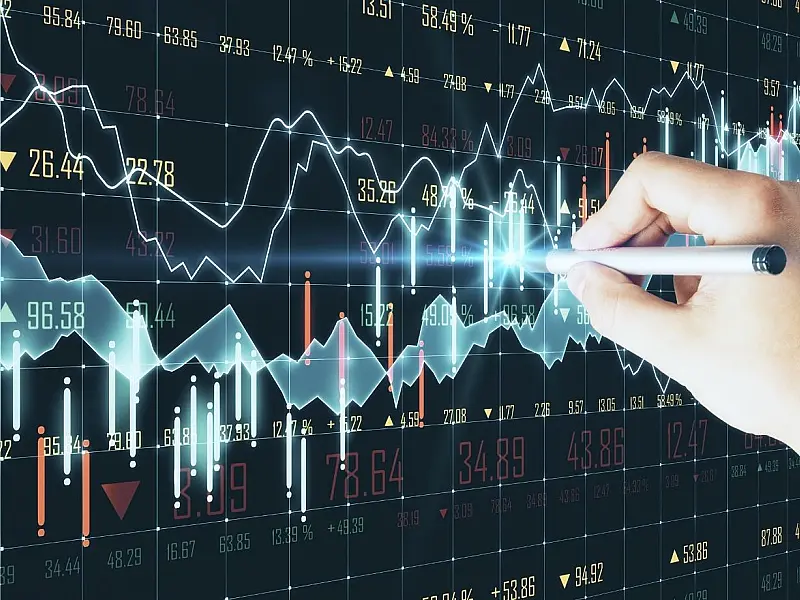 Monitor exibindo gráficos de barras e linhas ascendentes e descendentes em tons de azul e vermelho com dados econômicos.
