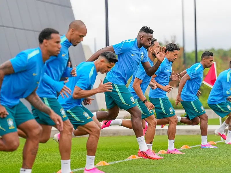 Grupo de jogadores da Seleção Brasileira perfilados no gramado verde durante atividade tática, ouvindo orientações de Carlo Ancelotti no centro do campo