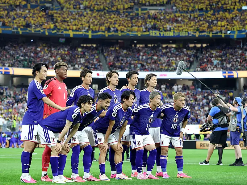 Jogadores da seleção do Japão vestindo o uniforme azul tradicional, correndo e se abraçando no centro do gramado em comemoração ao término da partida