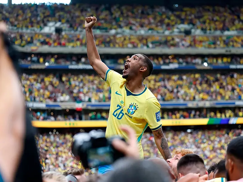 O jovem jogador Rayan, vestindo a camisa amarela da Seleção Brasileira, sorrindo e correndo de braços abertos no campo de futebol para celebrar a vitória sobre o Japão