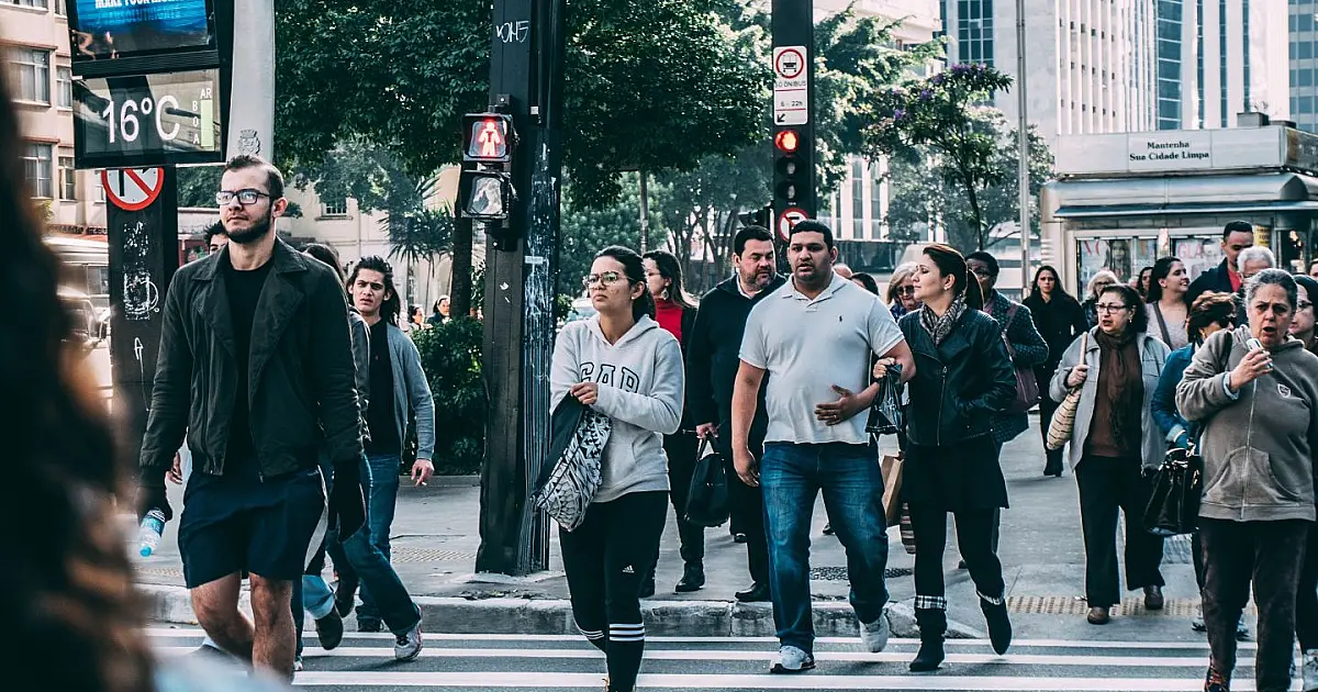Vista de pessoas caminhando em uma faixa de pedestres em ambiente urbano durante o dia, representando a circulação dos entrevistadores nas cidades