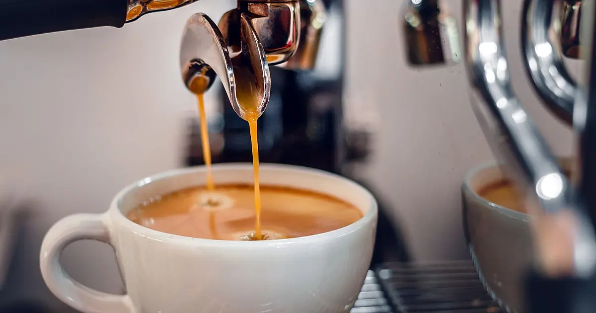 Extração de café expresso saindo de uma máquina profissional diretamente para uma xícara pequena de cerâmica