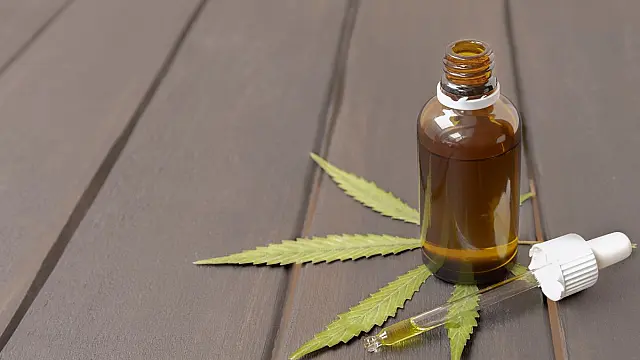Frasco de vidro com óleo de CBD e folha de cannabis sobre superfície de madeira.