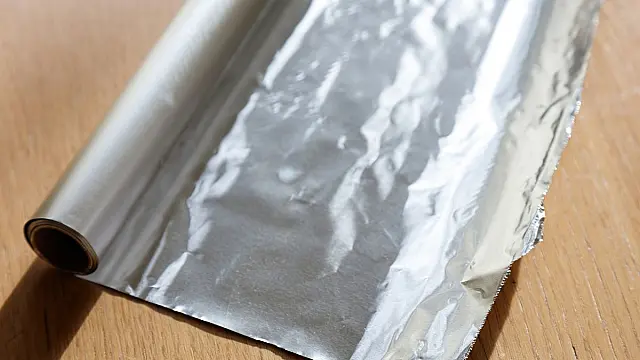 Rolo de papel alumínio laminado parcialmente desenrolado sobre superfície neutra