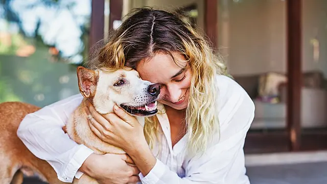 Mulher sorridente abraçando seu cachorro de estimação com carinho em ambiente acolhedor