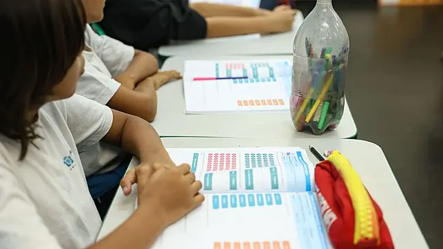 Estudante sentado em uma carteira dentro de uma sala de aula de escola pública.