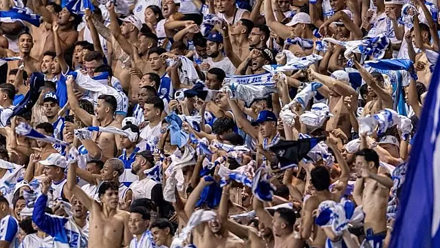 Torcedores vestindo azul e branco acenando bandeiras nas arquibancadas do estádio