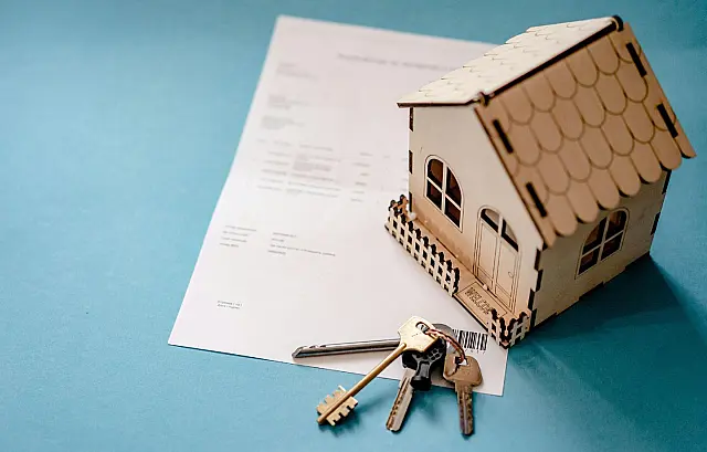 Maquete de madeira em formato de casa ao lado de chaves e papéis de contrato sobre superfície de madeira