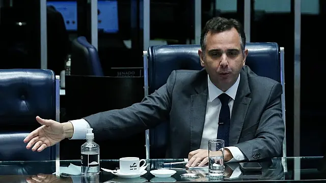 O senador Rodrigo Pacheco em pé discursando em um microfone formal em ambiente institucional.